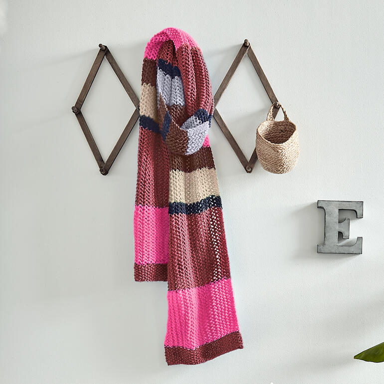 Bunter Schal aus NewWool auf einem gestreiften Hintergrund aufgehängt.