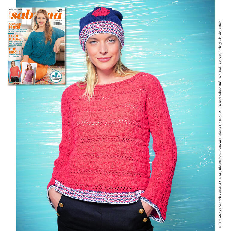 Frau in rotem Zopfmusterpullover mit passender Mütze vor buntem Hintergrund.