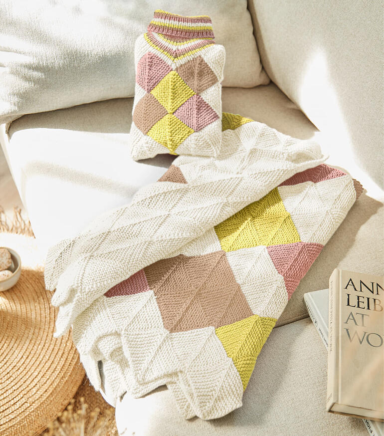 Babydecke und Wärmflaschenhülle mit geometrischem Muster auf einer Couch.