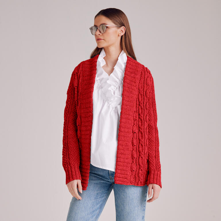 Frau in roter Jacke mit Zopfmuster steht vor neutralem Hintergrund.