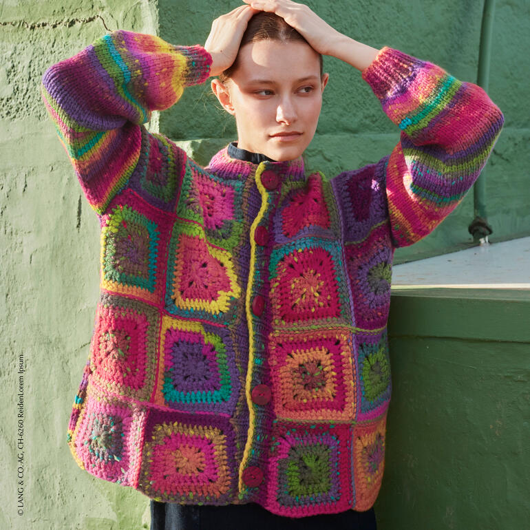 Frau trägt eine Jacke mit bunten Quadraten aus Mystery, hält sich die Hände an den Kopf.