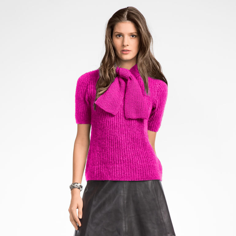 Frau trägt einen pinken Pullover mit breitem Schal, kombiniert mit einem Rock.