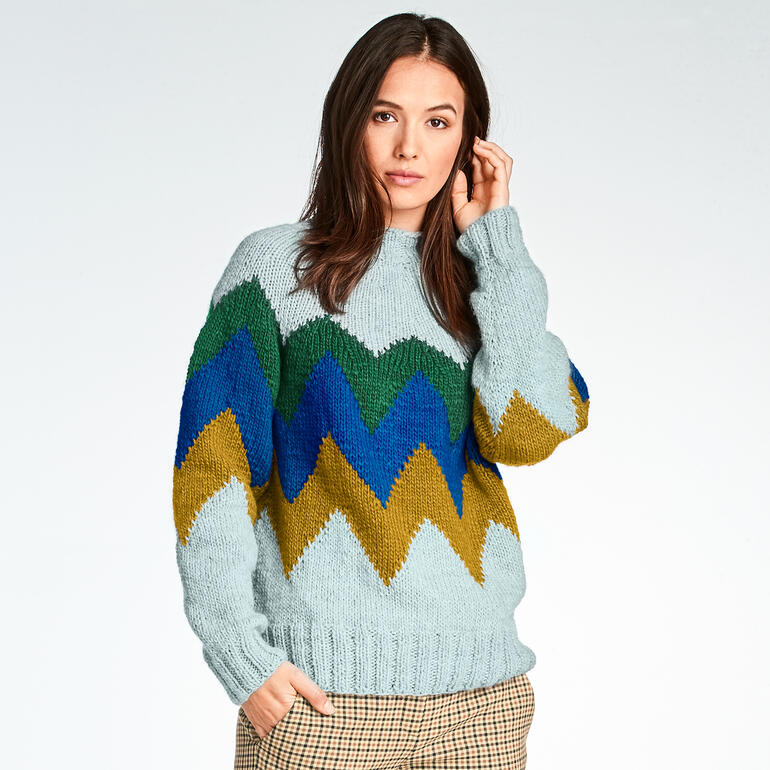 Frau in einem mintgrünen Pullover mit Zickzack-Muster in Blau und Gold.