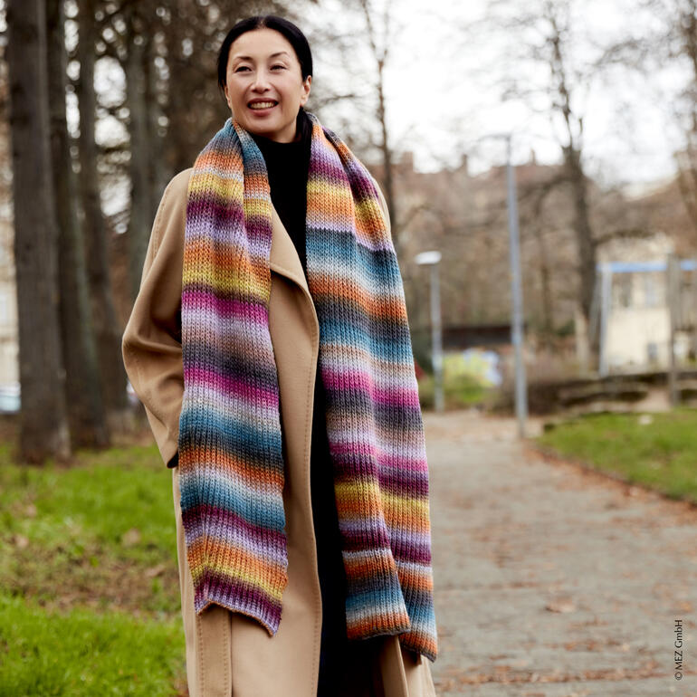 Frau trägt einen gestreiften Schal aus Virtuoso Color von Regia in einem Park.
