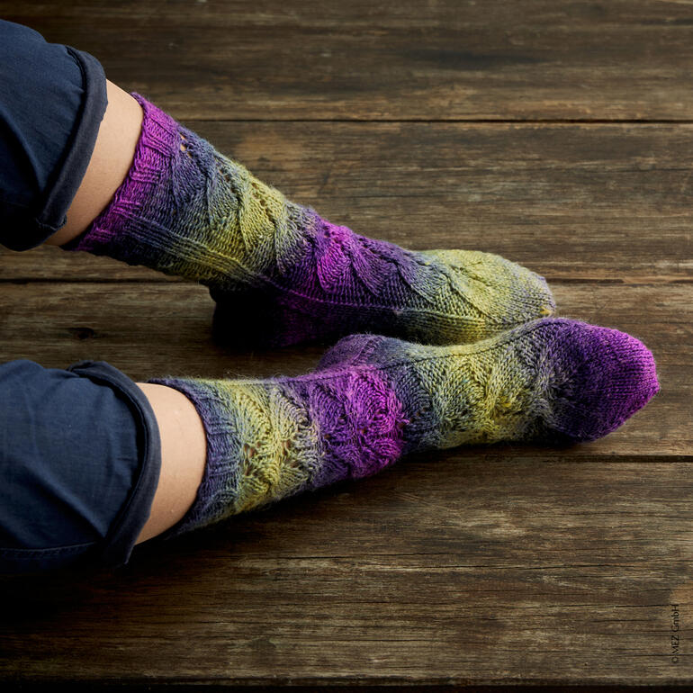 Füße in handgestrickten Socken aus Virtuoso Color von Regia auf Holzfußboden.