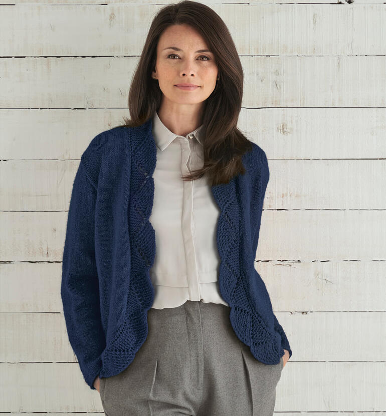 Frau trägt eine dunkelblaue Jacke mit Spitzenmuster auf einem Holz-Hintergrund