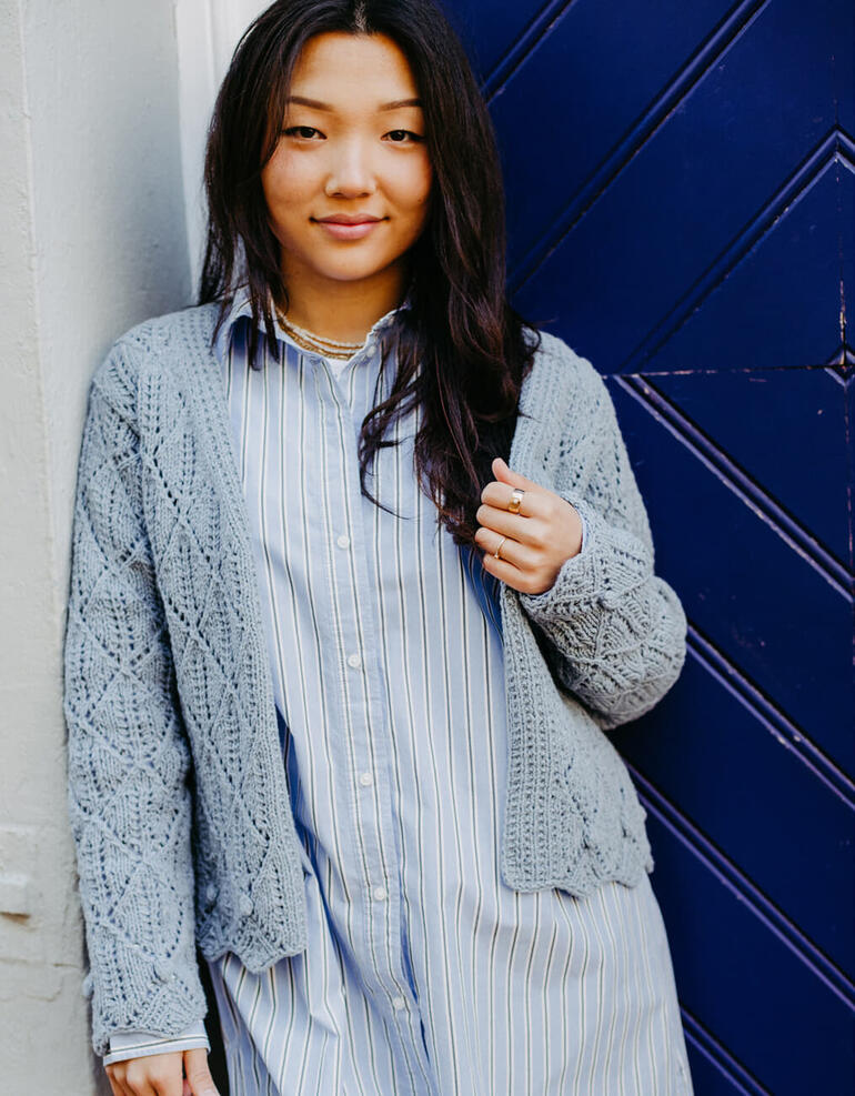 Frau in grauer Jacke mit Spitzenmuster auf einem blauen Hintergrund