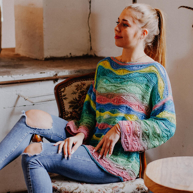 Frau in buntem Pulli mit Wellenmuster auf einem Stuhl in einem Raum