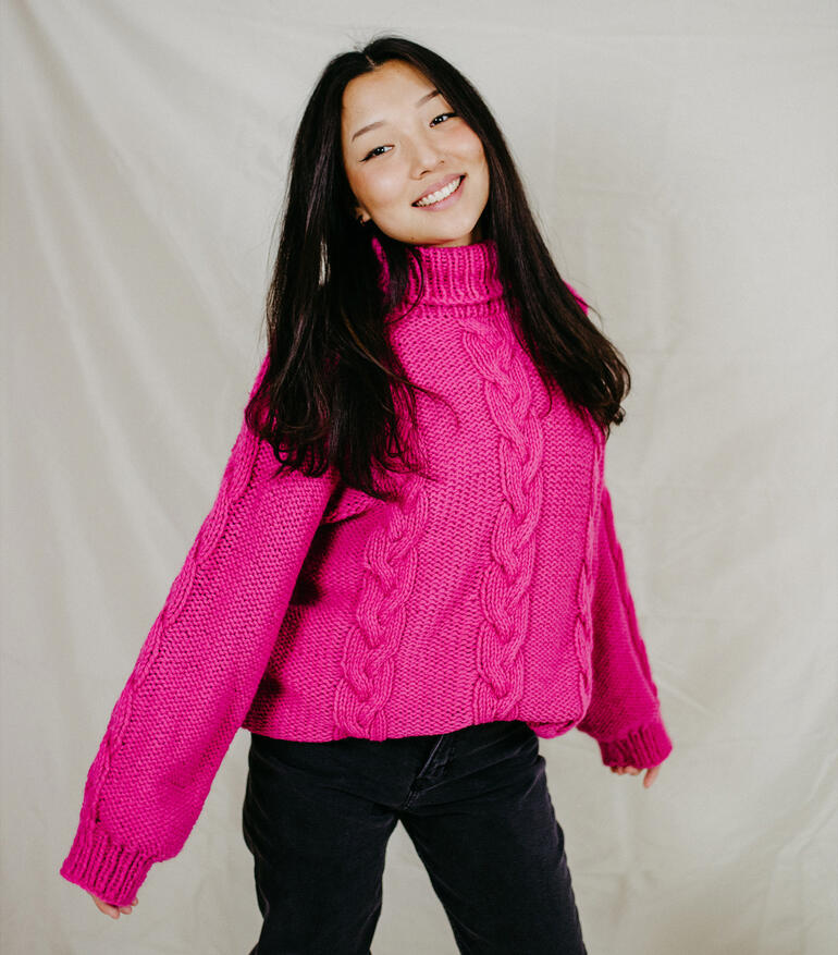 Frau in einem pinkfarbenen Rollkragenpullover mit Zopfmuster