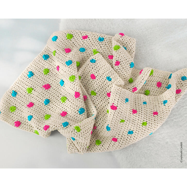 Häkelbabydecke in Creme mit bunten Punkten auf weichem Hintergrund