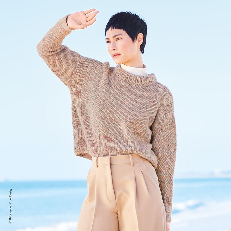 Brauner Pullover aus Alpaca am Strand getragen von einer Frau.