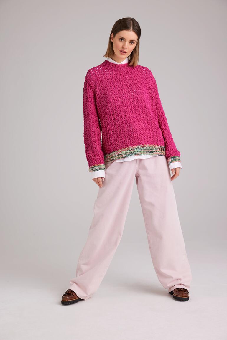 Fuchsiafarbener Pullover aus Merino, getragen von einer Frau in großen Hosen.