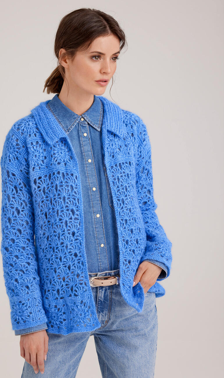 Helle gehäkelte Jacke in Blau, getragen von einer Frau mit Jeans.