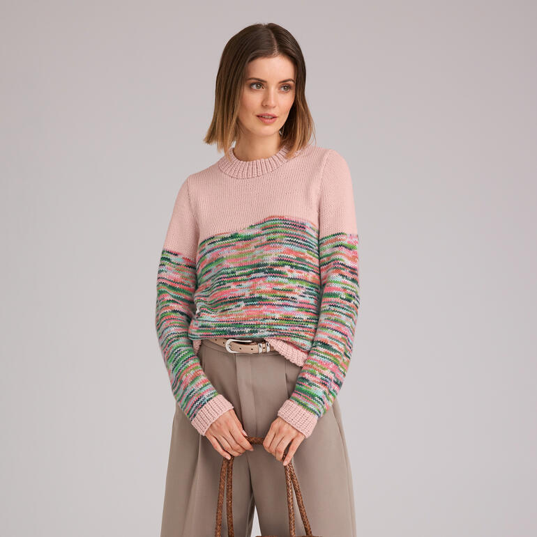 Gestreifter Pullover aus Merino-Print in sanften Farben, getragen von einer Frau, die lächelt.