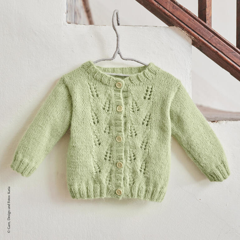 Grüne Babyjacke aus Soft Gratté mit Knöpfen, an einem Treppengeländer hängend.