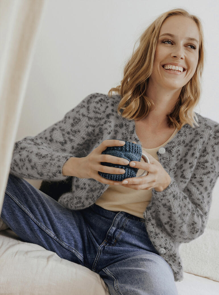 Grau gepunktete Jacke aus Phil Léo, lächelnd mit Tasse in der Hand.