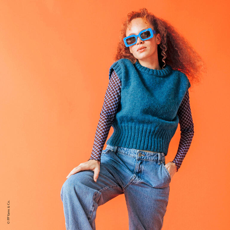 Blauer Pullunder aus Pingo Queen, lässig in Pose auf orangefarbenem Hintergrund.