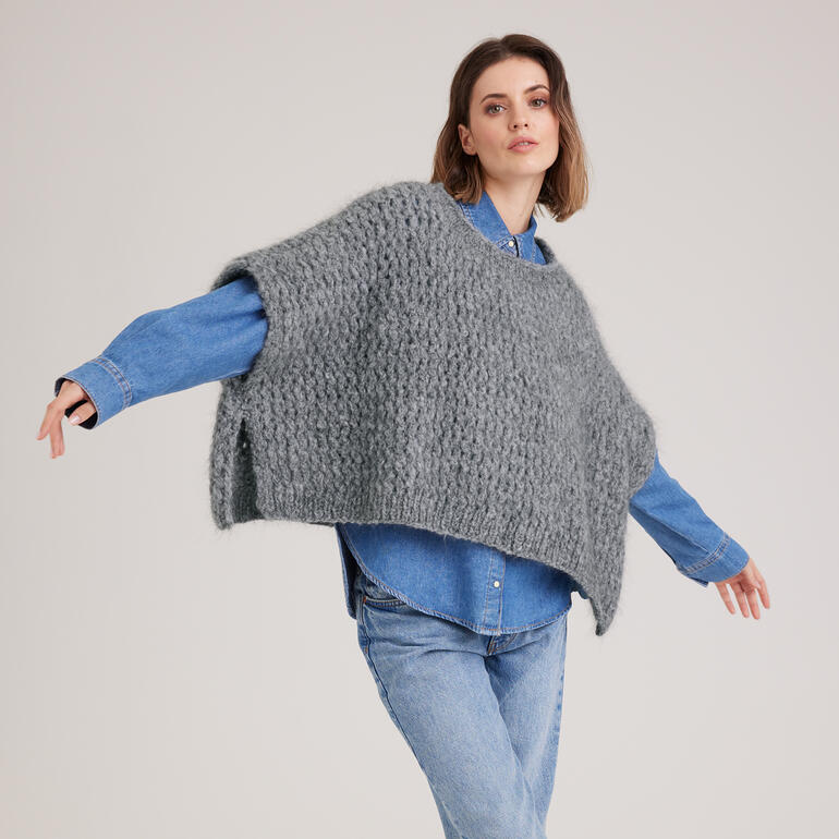 Grauer Poncho aus Nappy, elegant um die Schultern geworfen in Bewegung.