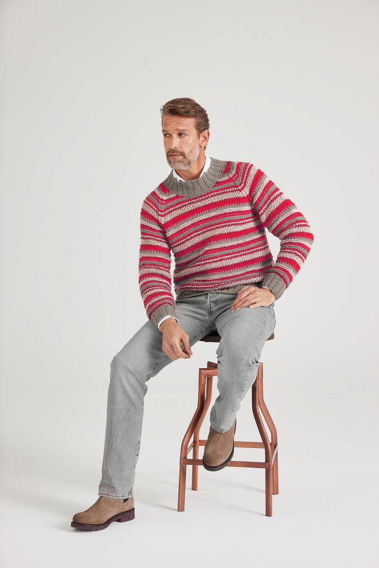 Mann sitzt auf einem Hocker, trägt gestreiften Herrenpullover in Rot und Grau.