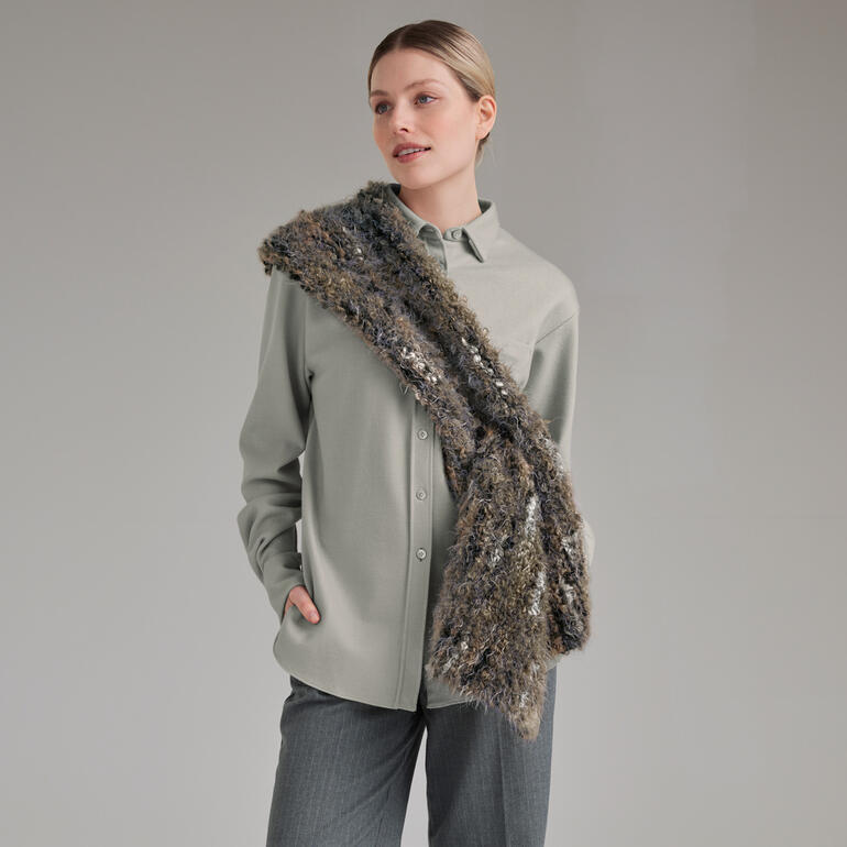 Frau trägt eine graue Bluse mit einem schimmernden braunen Stola, posiert vor neutralem Hintergrund.