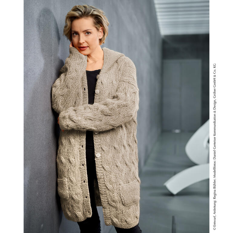 Frau sitzt in einer Long-Jacke aus Merino Super Kid in moderner Umgebung.