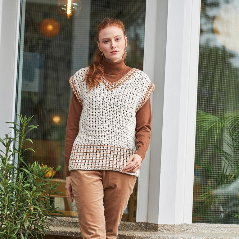 Frau trägt einen hellen, gehäkelten Pullunder und steht vor einem Fenster.