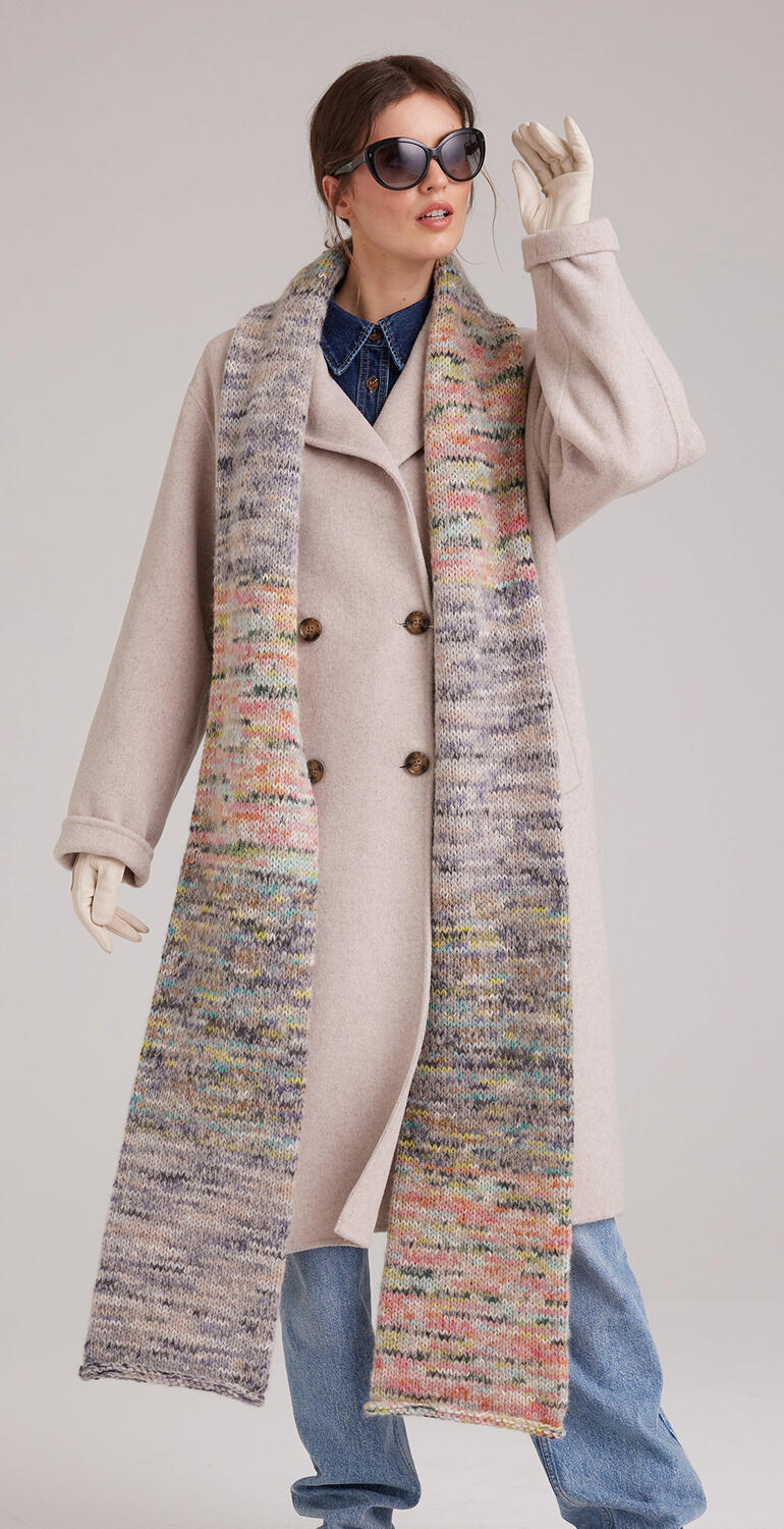 Frau in beiger Jacke trägt einen bunten Schal und Sonnenbrille für einen modernen Look.
