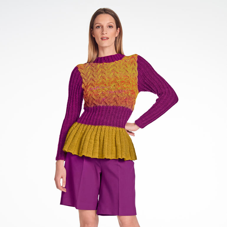 Frau in buntem Pullover mit Schößchen posiert vor einem weißen Hintergrund.