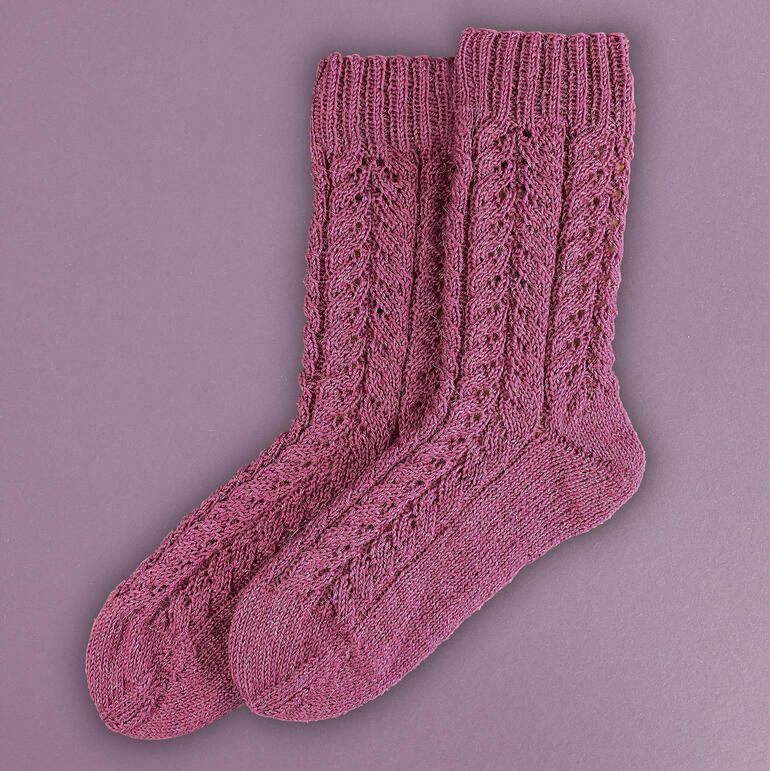 Rosa gestrickte Socken mit Zopfmuster in verschiedenen Größen.