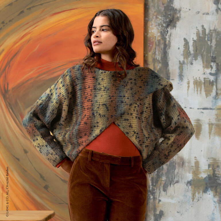 Frau trägt einen bunten Bolero-Pullover aus Cloud Tweed, vor einzigartigem Hintergrund