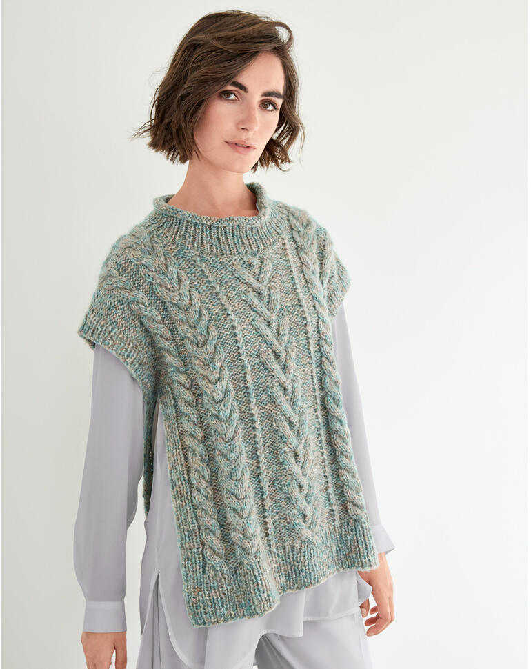 Modische Frau trägt einen Pullunder-Überwurf aus Frigga-Wolle, lächelnd vor neutralem Hintergrund