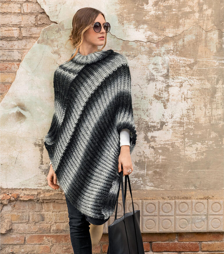 Frau trägt gestreiften Poncho in Schwarz und Grau mit Tasche in der Stadt.