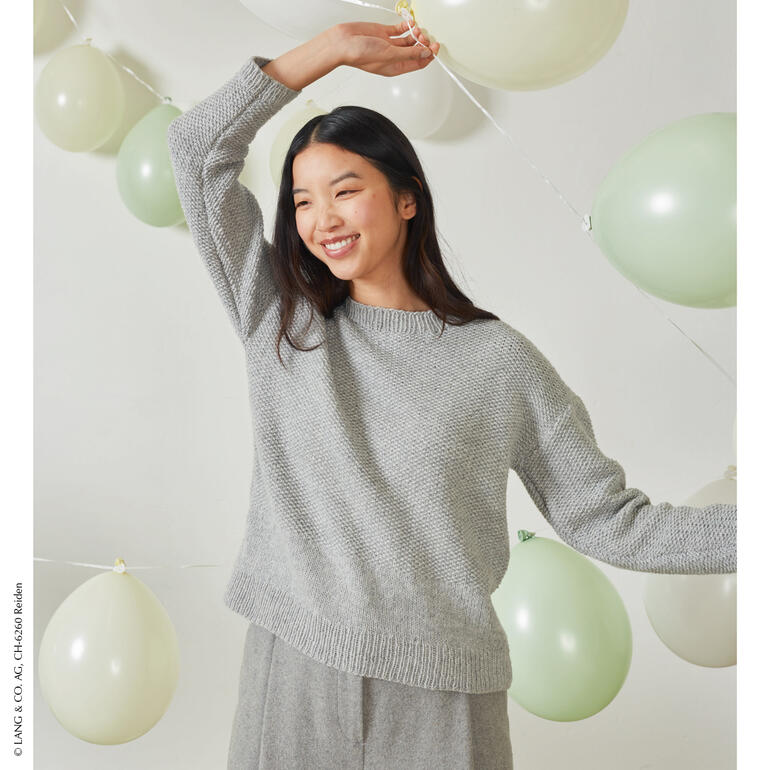 Frau trägt einen grauen Pullover aus Lambswool, lächelt glücklich.