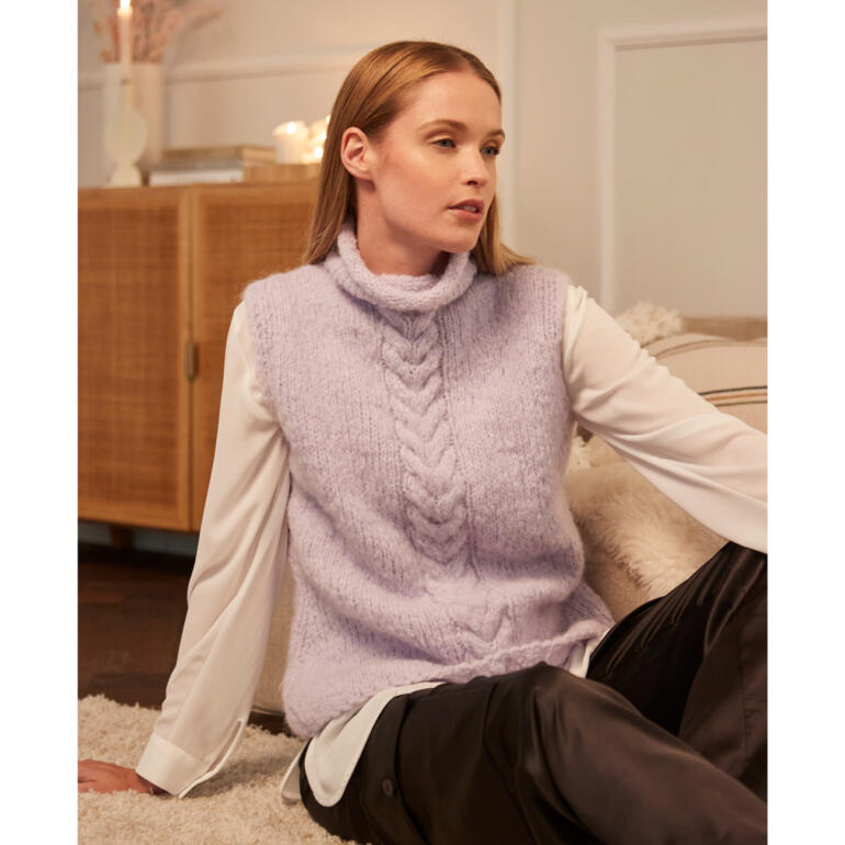 Frau sitzt in einem lila Pullunder aus Nappy, lächelt entspannt.
