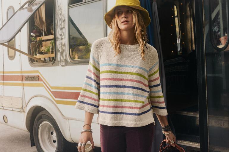 Frau in gestreiftem Pullover mit Hut, steht vor einem Wohnmobil.