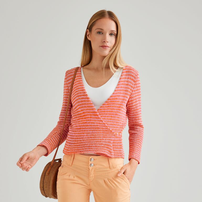 Frau in orangefarbenem Wickeljacke, lächelt in die Kamera.