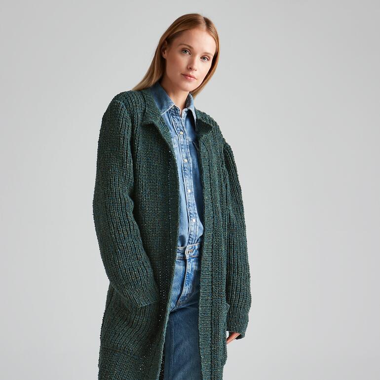 Frau in grünem Mantel steht lässig an einer Wand.