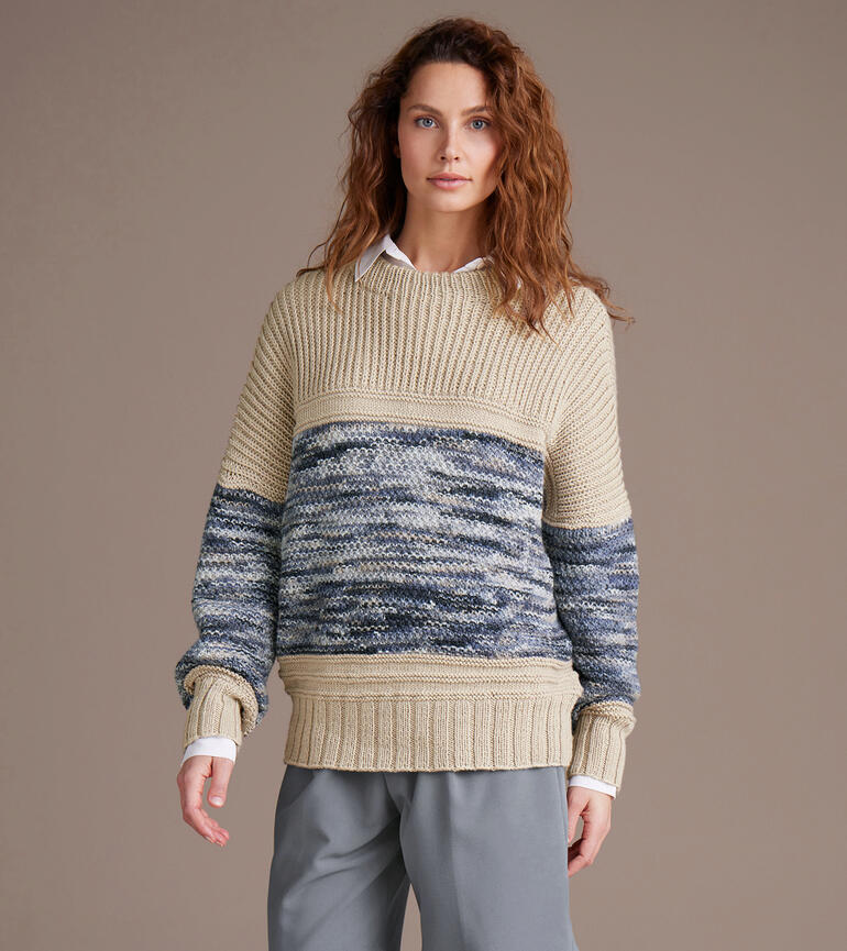 Frau in gemustertem Pullover mit langen Ärmeln steht vor einem neutralen Hintergrund.