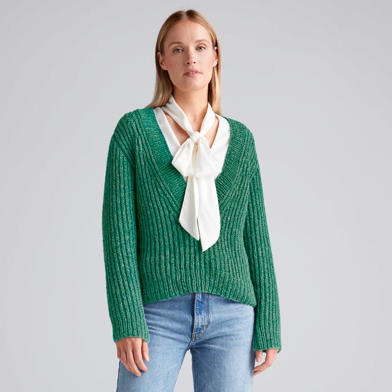 Grüner Pullover aus Punktino mit V-Ausschnitt und weißer Bluse darunter.