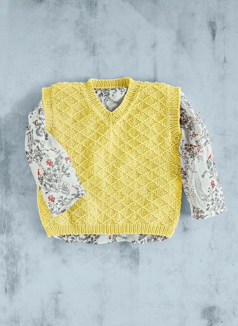 Gelber Kinderpullunder liegt flach über einem floralen Hemd aus Baumwolle.