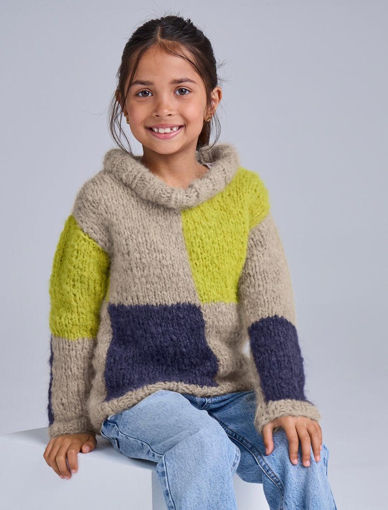 Bunter Kinderpullover aus Nappy mit verschiedenen Farbfeldern, fröhlich lächelnd.