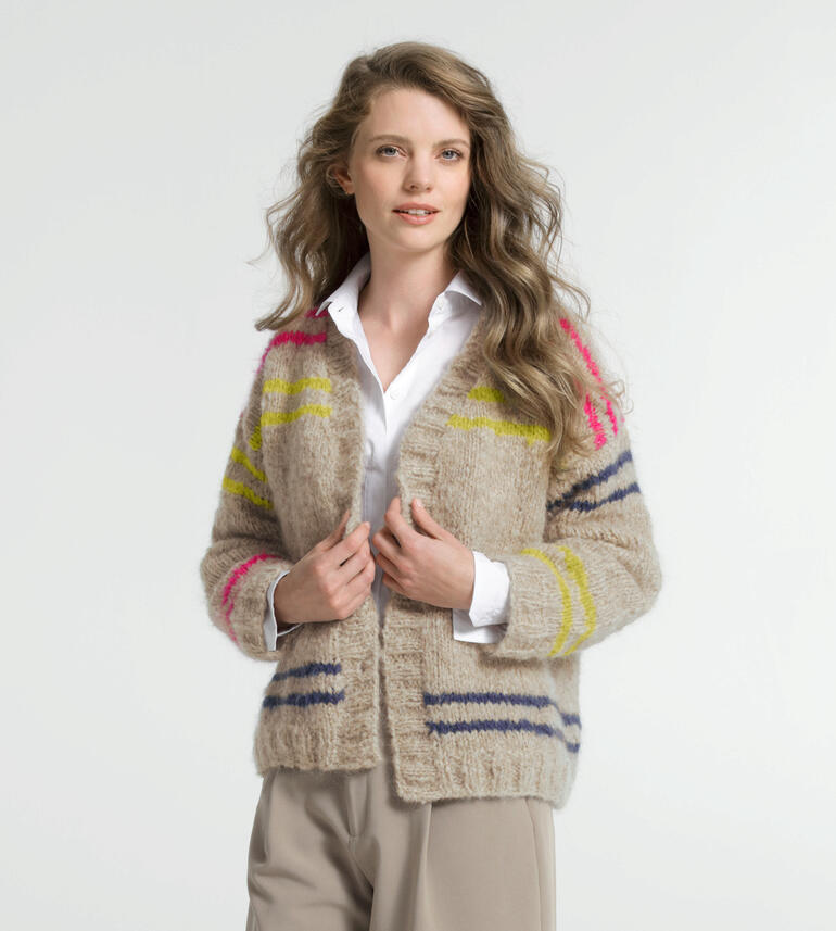 Jacke aus Nappy in beige mit bunten Streifen, getragen von einer Frau.