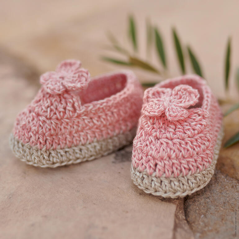 Zwei gehäkelte Babyschühchen mit Blumenmotiven auf Steinboden.