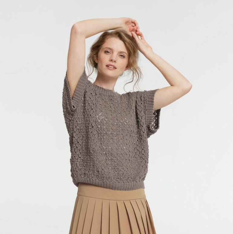 Frau in grauem Pullunder mit kurzer Ärmel vor heller Wand.