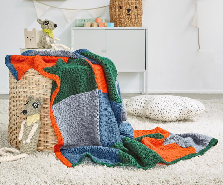 Bunte Kinderdecke liegt auf einem korbartigen Sitzmöbel.