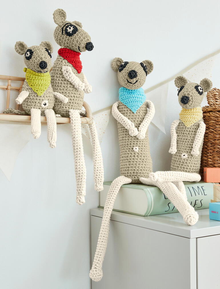 Vier gehäkelte Erdmännchen mit bunten Schals auf einem Tisch.