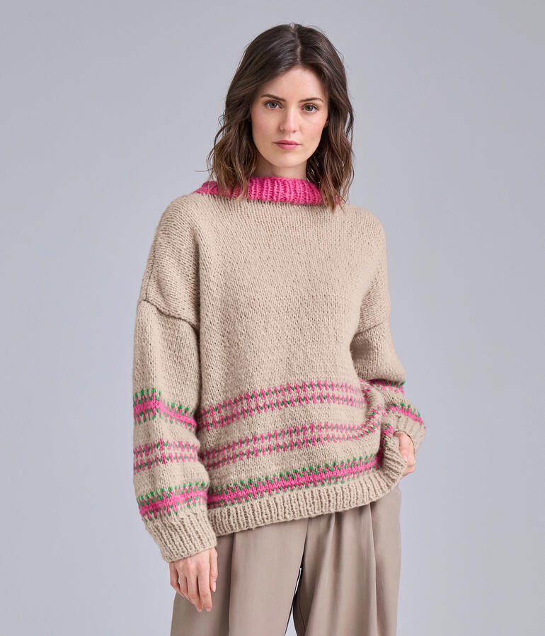 Pullover aus NewWool in Beige mit pinken Akzenten, getragen von einer Frau.