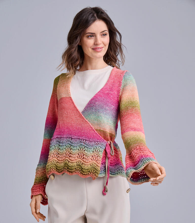 Frau in buntem Wickeljacke aus Pinterella lächelt vor grauem Hintergrund.