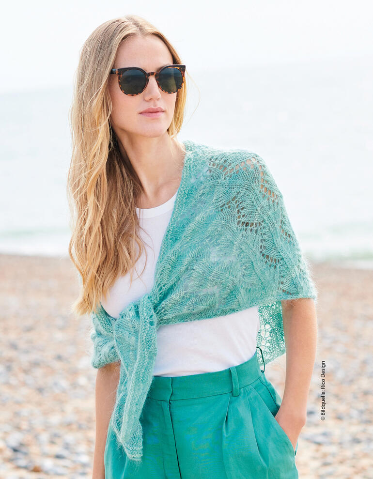 Frau in türkisfarbenem Dreiecktuch aus Merino und Mohair am Strand.