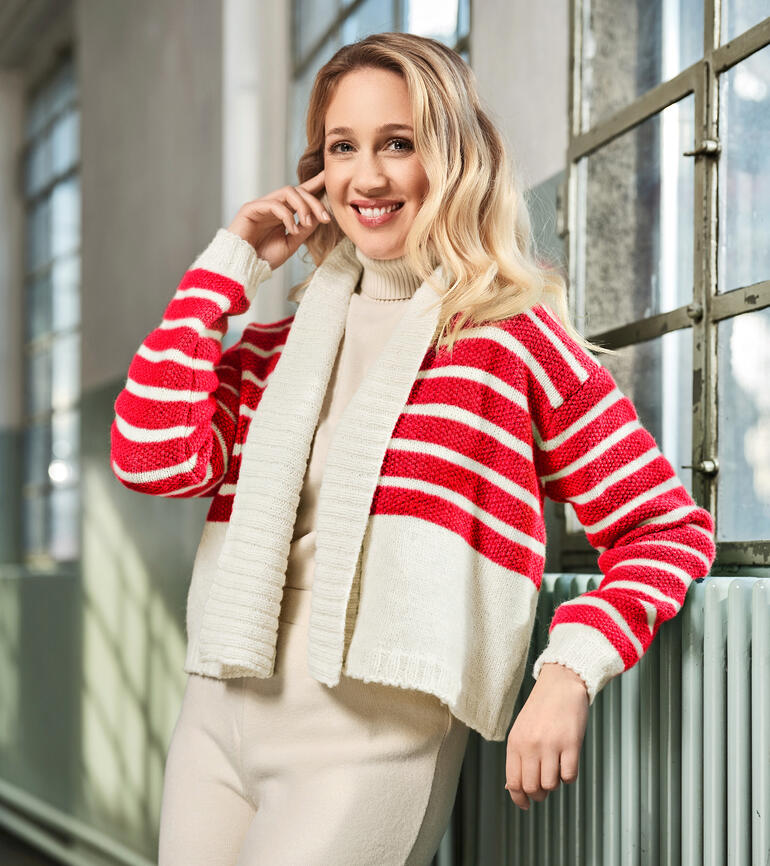 Frau in gestreiftem Cardigan aus Alpaka Deluxe, lächelt und posiert in einem Atelier.